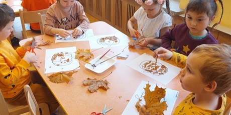 Powiększ grafikę: Dzieci wyklejają liśćmi szablon dyni.