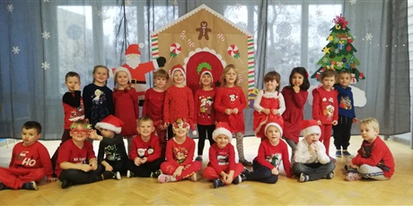 Powiększ grafikę: Dzieci ubrane na czerwono w czapkach mikołajowych na tle dekoracji Mikołajkowej.