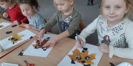 Powiększ grafikę: Dzieci wykonują pracę plastyczną z wykorzystaniem liści.