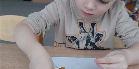 Powiększ grafikę: Dziecko wykonuje pracę plastyczną z wykorzystaniem liści.