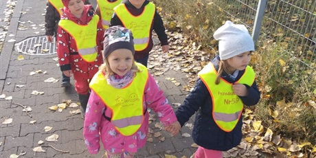 Powiększ grafikę: Dzieci na spacerze w drodze do biblioteki trze w kamizelki odblaskowe. Trzymają się za ręce.