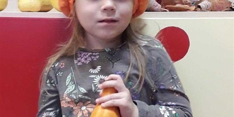Powiększ grafikę: Dziewczynka w pomarańczowej czapce-dyni z dynią w rękach.