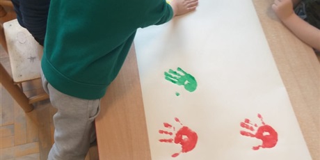 Powiększ grafikę: Chłopiec odbija pomalowaną dłoń na dużym formacie papieru.