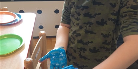 Powiększ grafikę: Chłopiec maluje dłoń niebieską farbą.