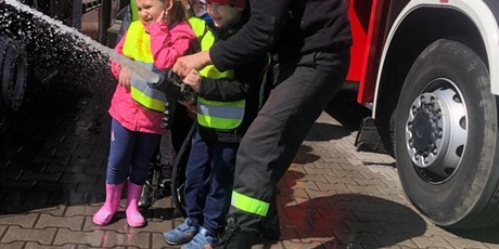 Powiększ grafikę: Dzieci puszczają wodę z węża strażackiego.