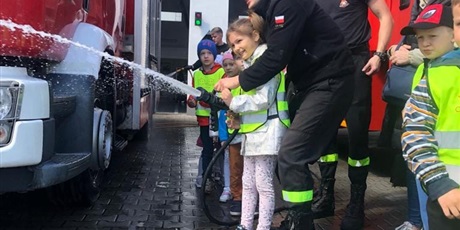 Powiększ grafikę: Dzieci puszczają wodę z węża strażackiego.