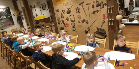 Powiększ grafikę: Dzieci siedzą przy długim stole w materiałami plastycznymi do wykonania latawców.