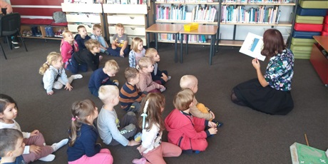 Powiększ grafikę: Dzieci słuchają czytanej książki przez panią w bibliotece.