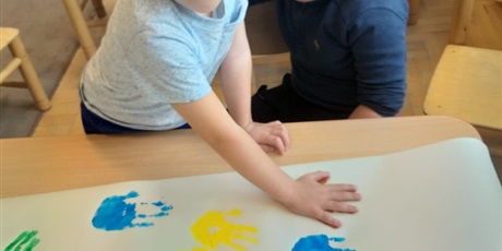 Powiększ grafikę: Chłopiec odbija pomalowaną dłoń na dużym formacie papieru.